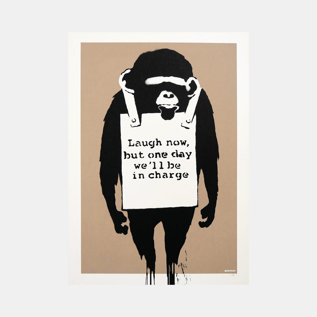 A black ape figure stands with both arms hanging at its sides, wearing a white sandwich board bearing the words "Laugh now, but one day we'll be in charge" against a brown background.