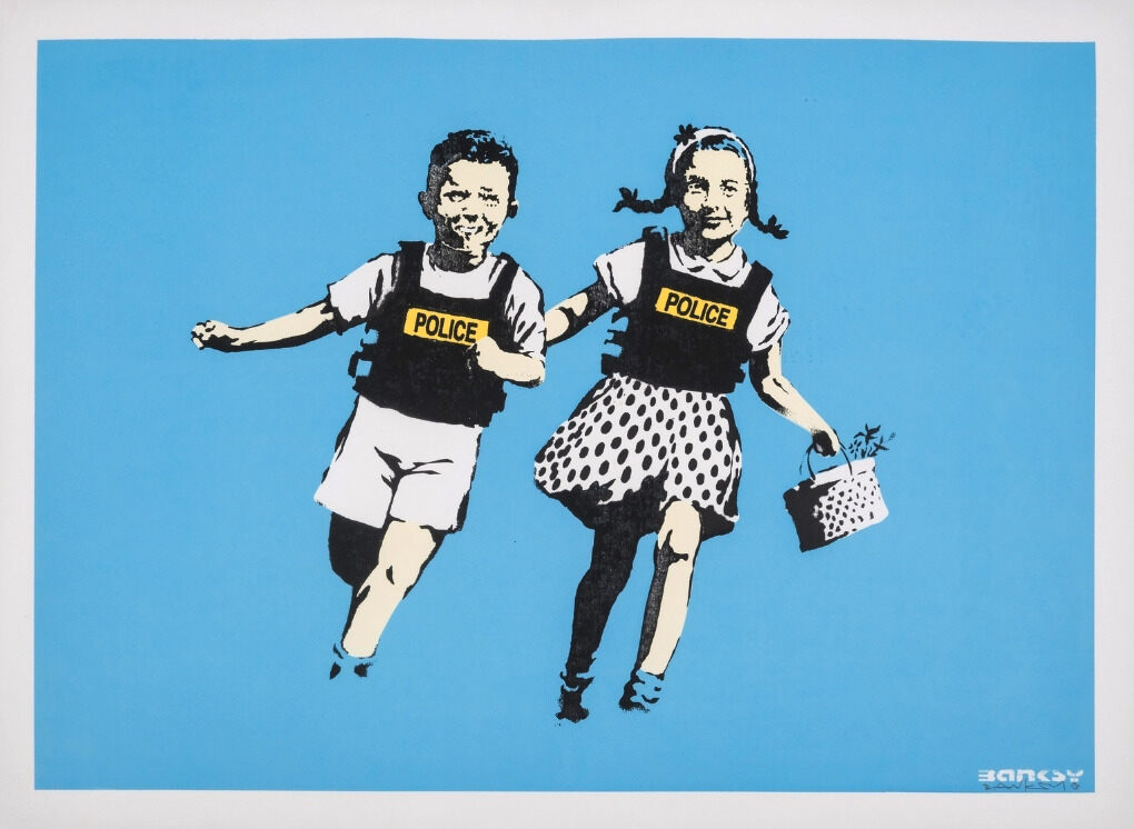 Two smiling children in black POLICE vests run hand in hand against a bright blue background.