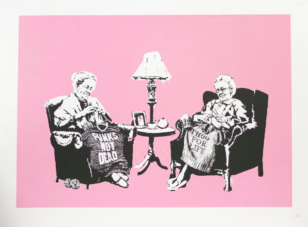 Two elderly women sit in armchairs knitting jumpers bearing PUNKS NOT DEAD and THUG FOR LIFE, with a small table and lamp between them, against pink.