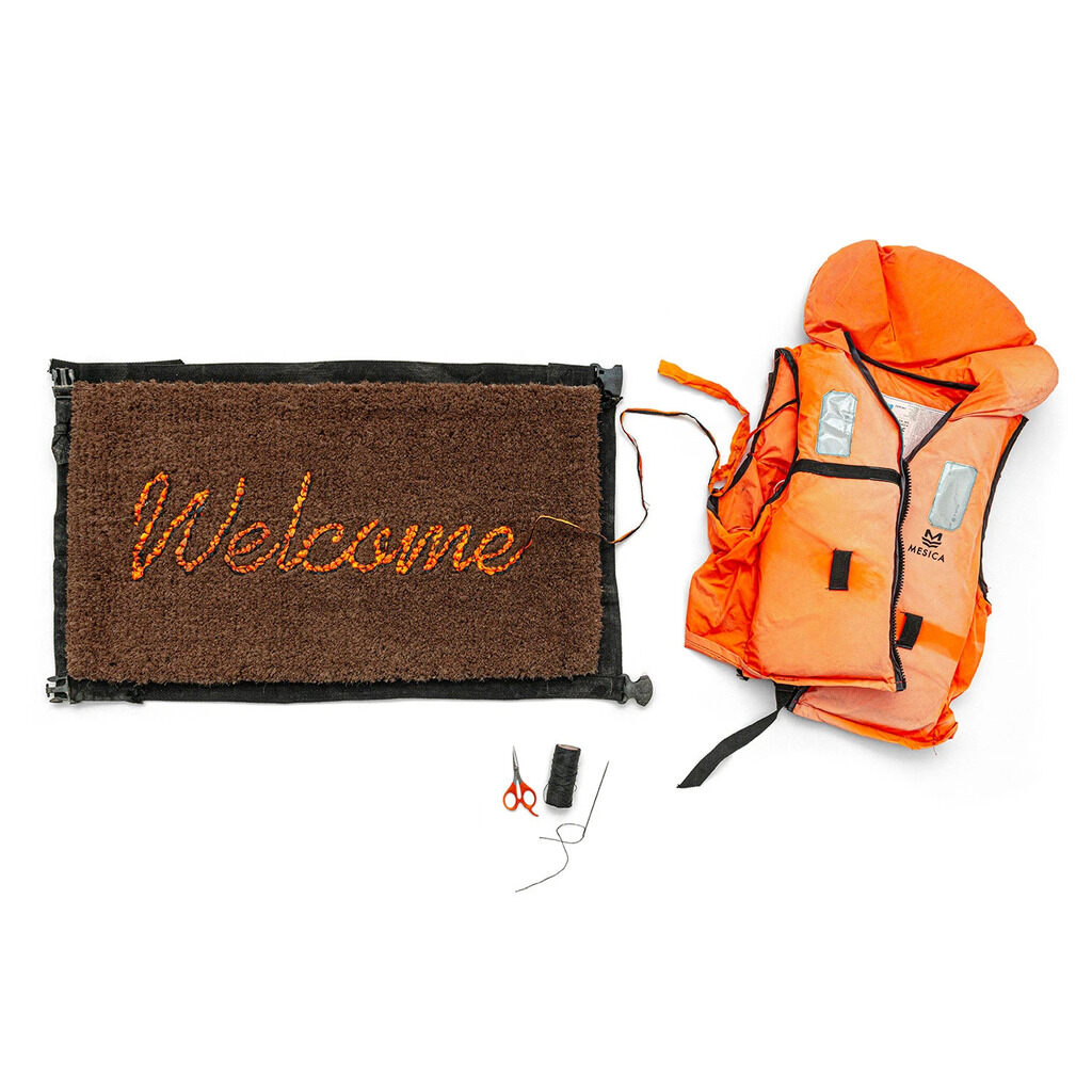 Brown Welcome doormat beside an orange life jacket, scissors and sewing materials on white.
