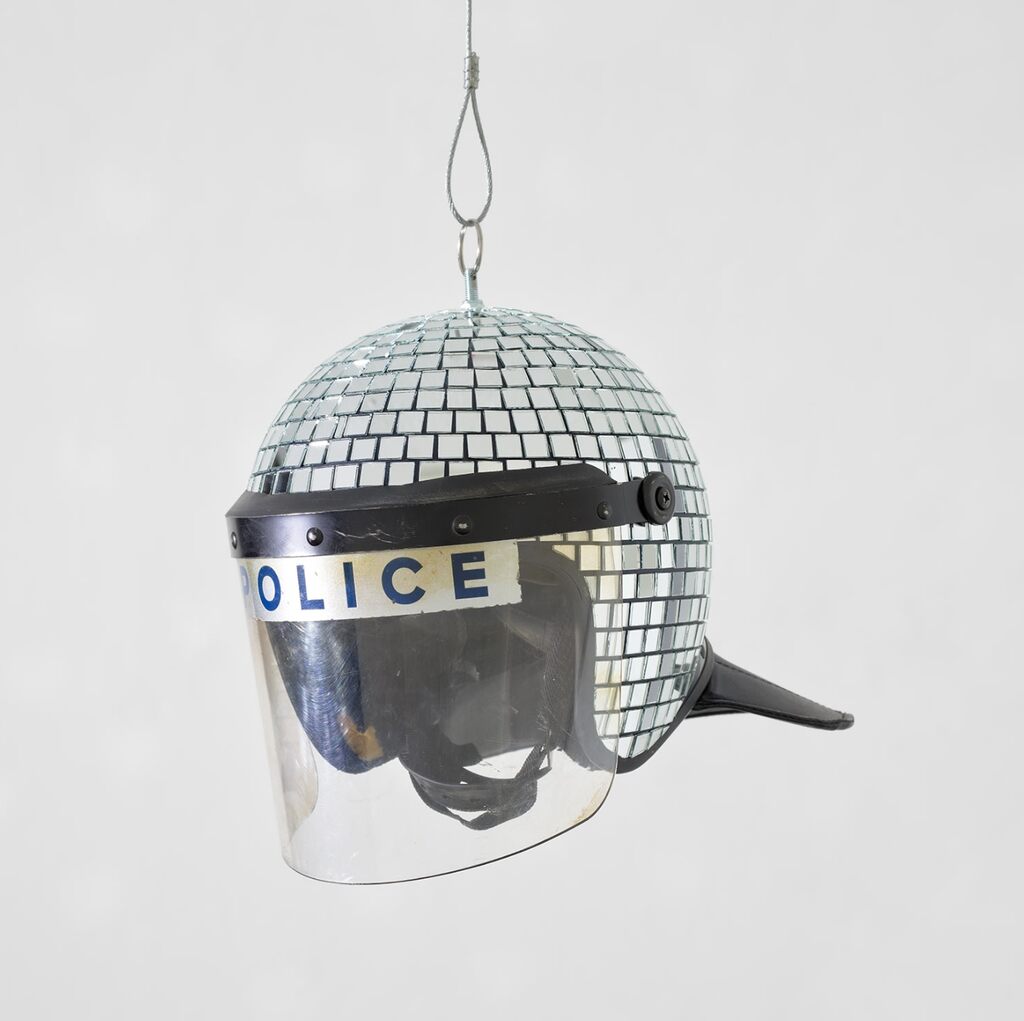 Um capacete de polícia espelhado com viseira transparente pendurado por uma alça.
