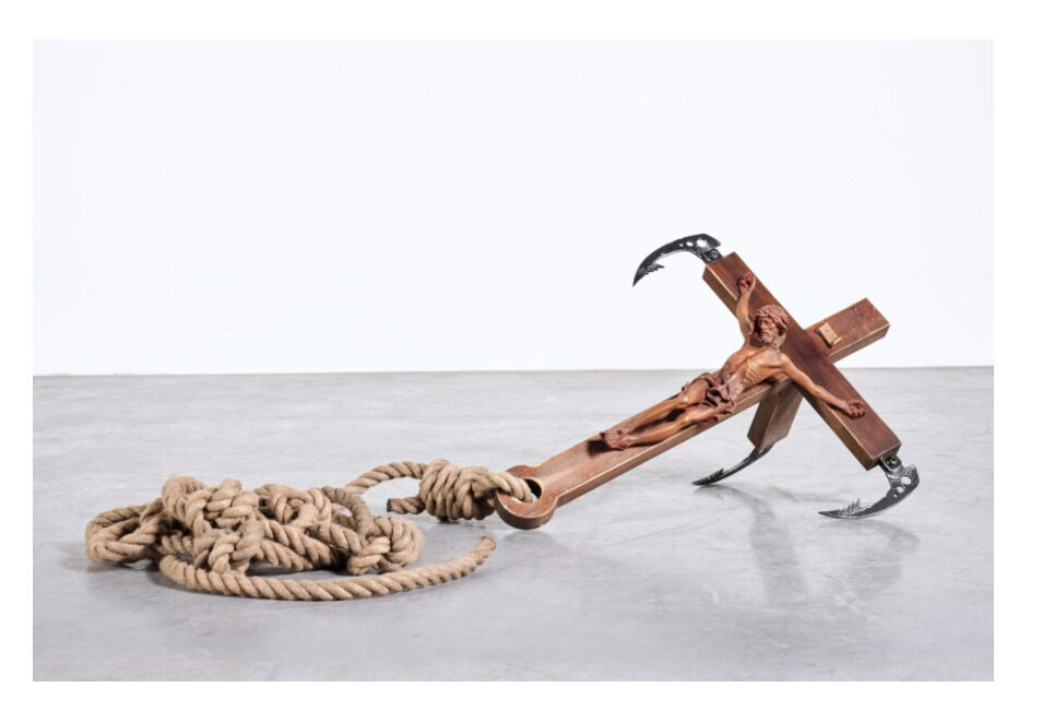 A wooden cross-shaped object with curved metal hooks lies beside a coiled rope.