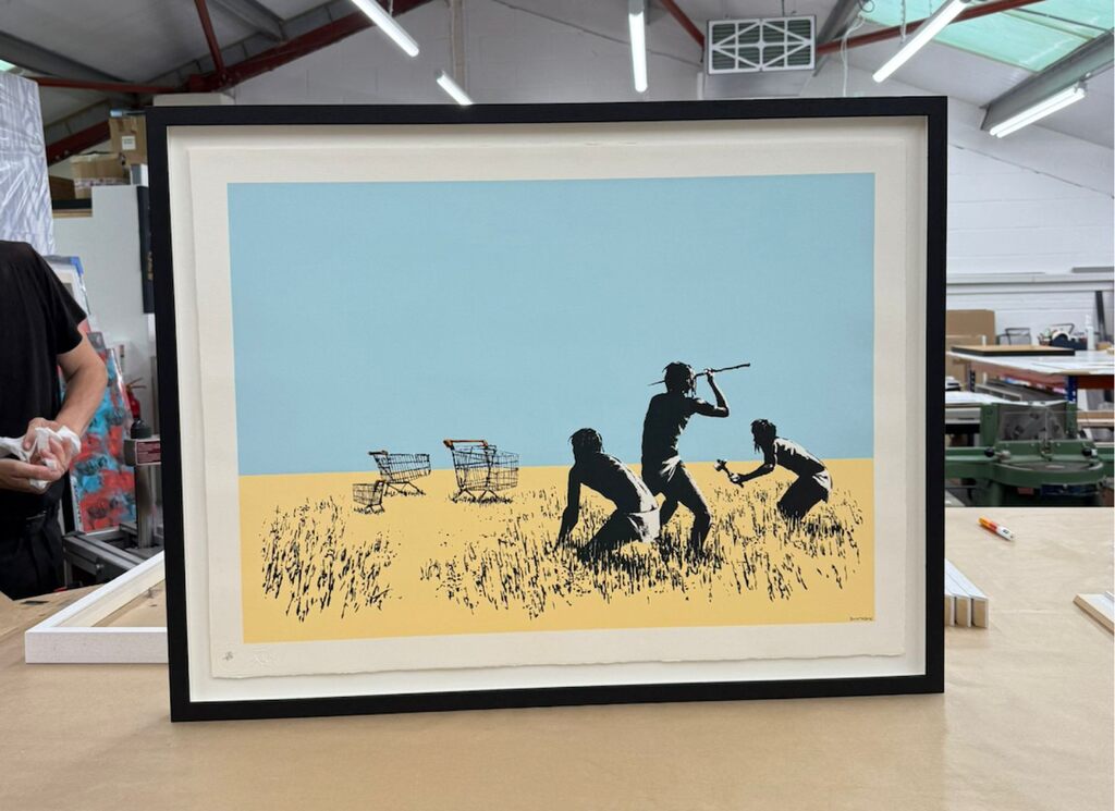 Framed shopping-cart hunting scene in yellow and blue on a workbench.