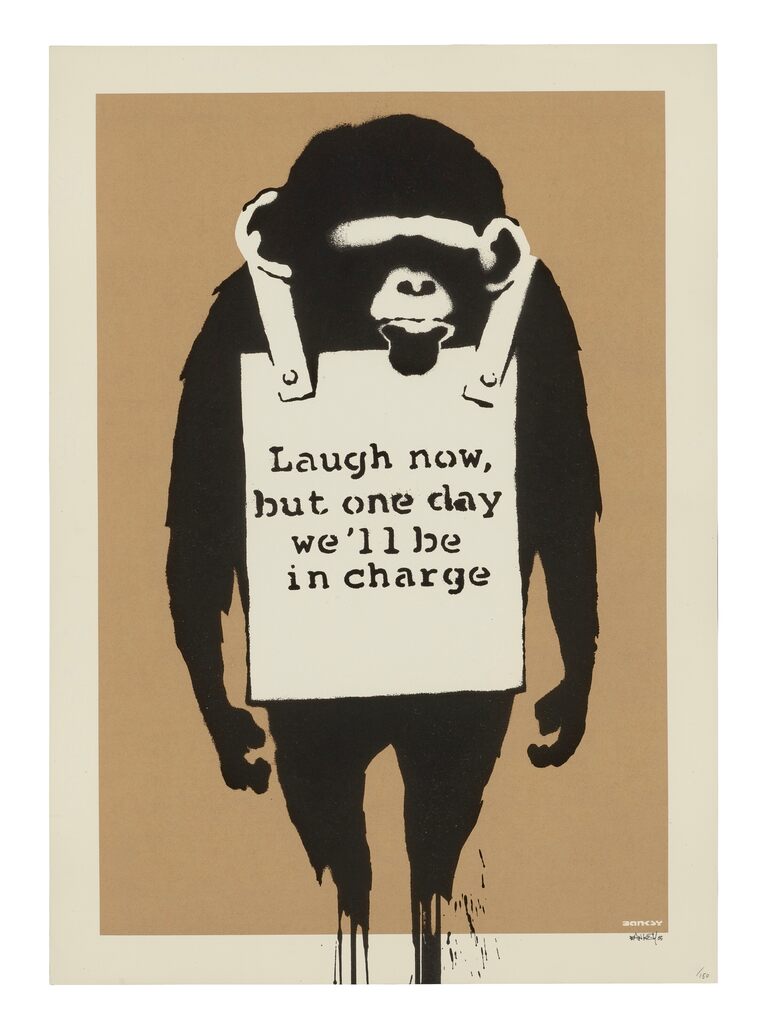 A black ape figure stands with both arms hanging at its sides, wearing a white sandwich board bearing the words "Laugh now, but one day we'll be in charge" against a brown background.