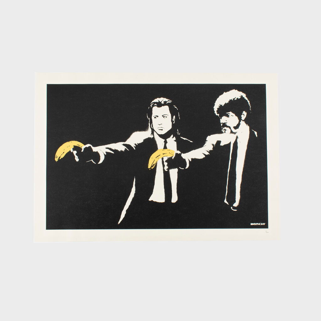 Against a black background, two male figures in black suits and white shirts have arms extended while holding yellow bananas, one banana angled left and another positioned lower near the right.