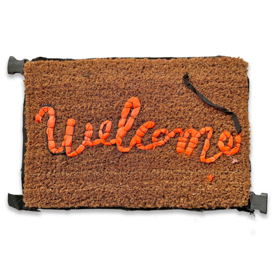 A brown doormat with orange Welcome script and black straps.