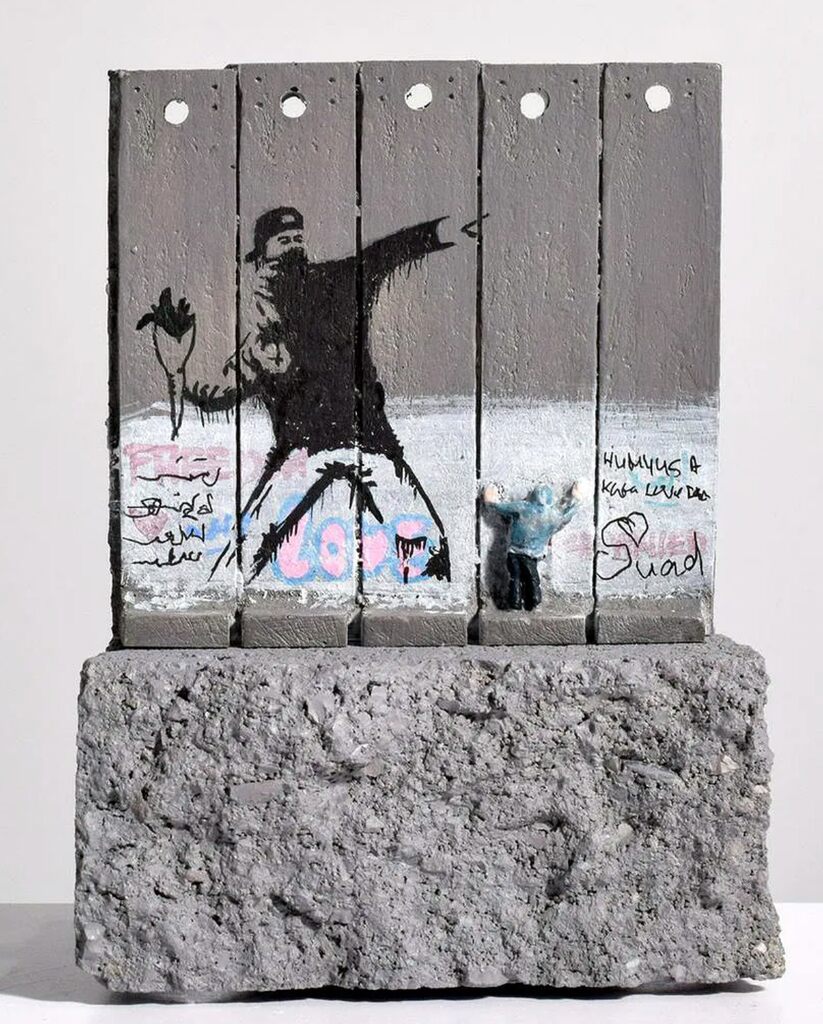 Small grey panelled wall model with a flower-throwing figure and graffiti, mounted on a rough grey base.