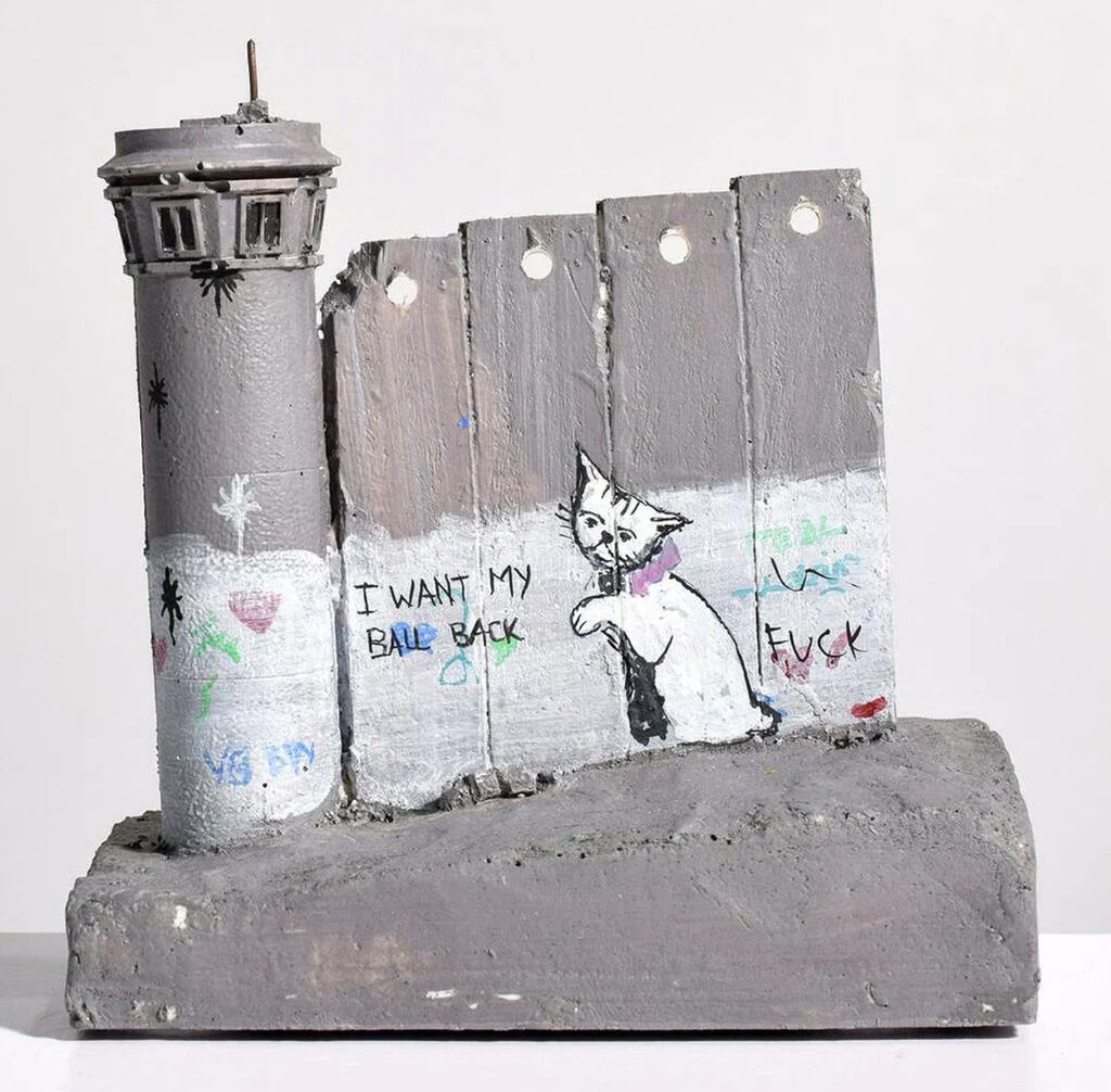 A small wall-and-watchtower model bears graffiti, a rat figure and I Want My Ball Back lettering.